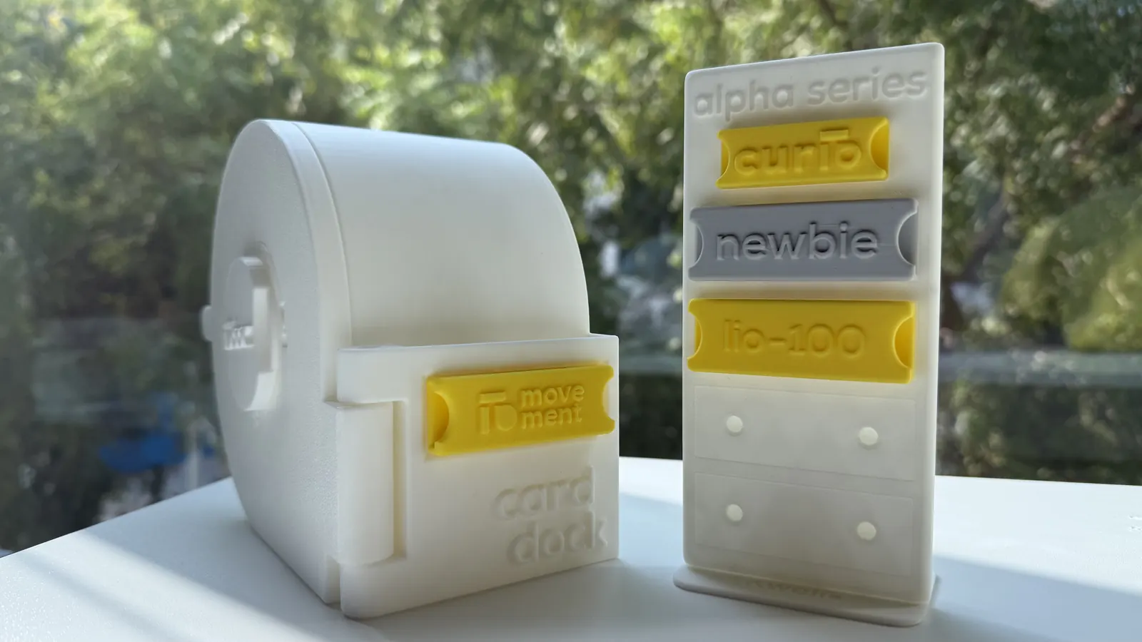 A white LioBox with a yellow badge in the card dock on its front, beside a badge rack holding three more badges