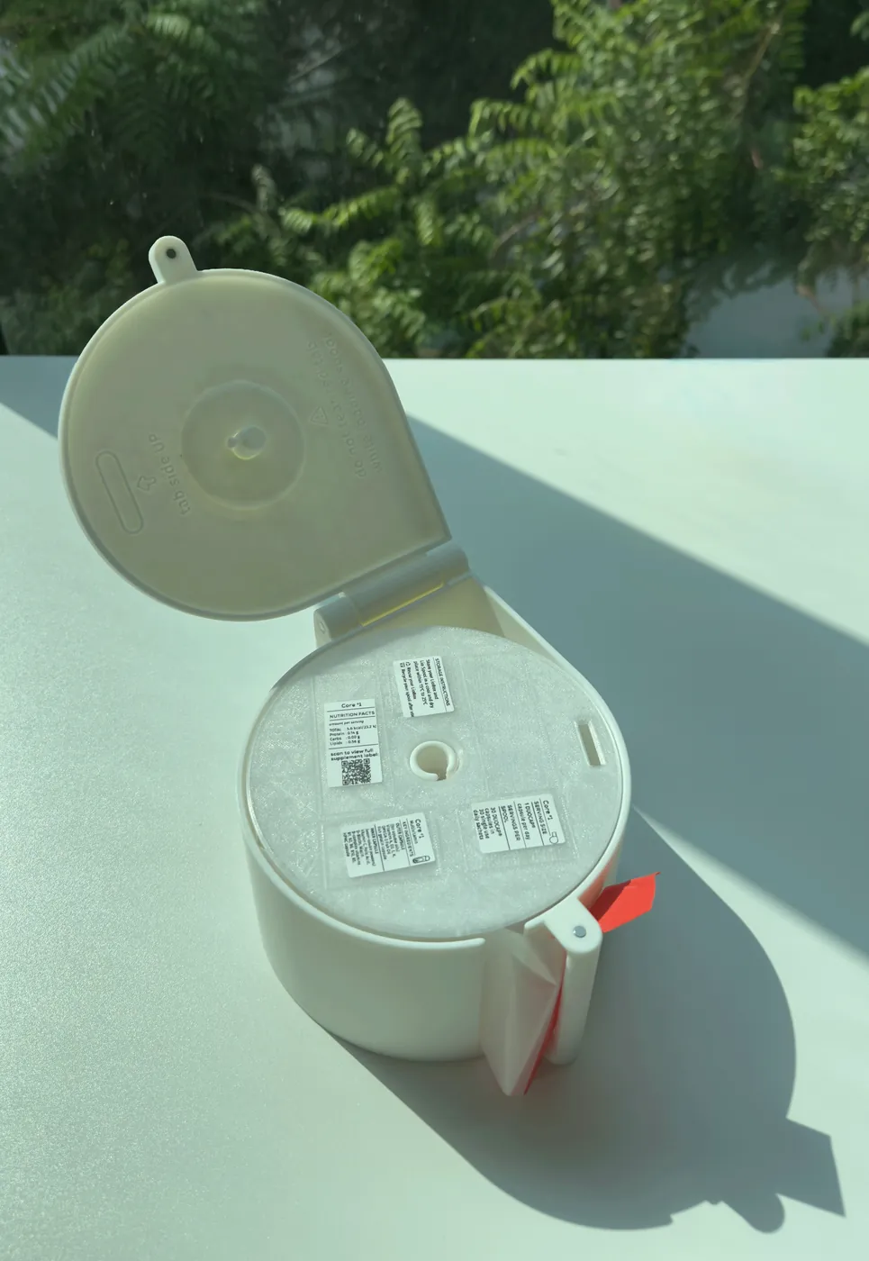 A loaded LioBox in sunlight, with a strip of daily sachets coming out of its slot